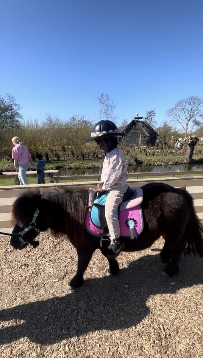 Een kind met een cap rijdt op een shetlandpony